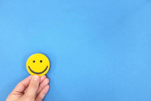 Hands holding a yellow smiley face in blue background with copy space. Positivity and happiness concept. Hands holding a yellow smiley face in blue background with copy space. Positivity, good customer feedback and happiness concept. anthropomorphic smiley face photos stock pictures, royalty-free photos & images