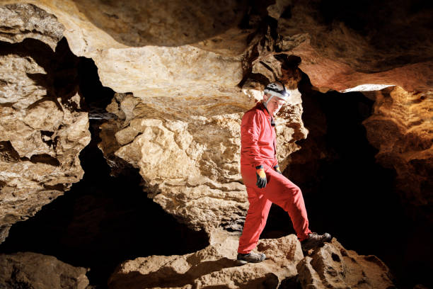 istock Man walking and exploring dark cave with light headlamp underground. Mysterious deep dark, explorer discovering mystery moody tunnel looking on rock wall inside. 1250123876