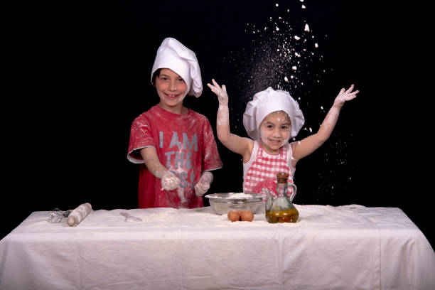 children playing to be cooks, playing with flour and throwing it themselves, with a black background young boy and girl