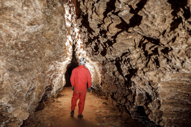 istock Man walking and exploring dark cave with light headlamp underground. Mysterious deep dark, explorer discovering mystery moody tunnel looking on rock wall inside. 1250124592