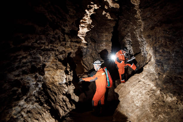 istock Two men, strong physique, explore the cave. Men dressed in special clothes to pass through the cave and stopped, looking at the map 1250124701