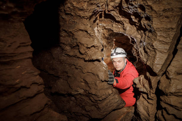 istock Man walking and exploring dark cave with light headlamp underground. Mysterious deep dark, explorer discovering mystery moody tunnel looking on rock wall inside. 1250124918