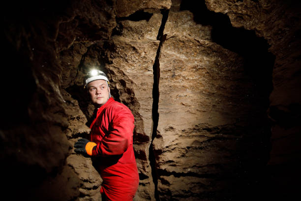 istock Man walking and exploring dark cave with light headlamp underground. Mysterious deep dark, explorer discovering mystery moody tunnel looking on rock wall inside. 1250125080
