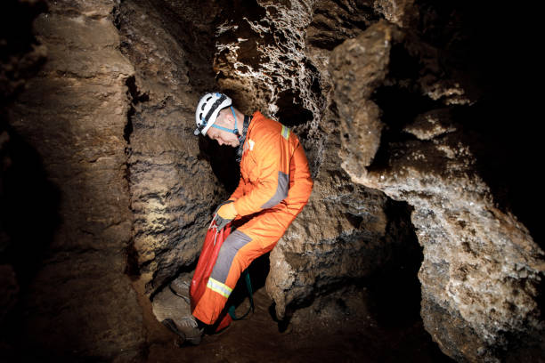 istock Man walking and exploring dark cave with light headlamp underground. Mysterious deep dark, explorer discovering mystery moody tunnel looking on rock wall inside. 1250125186