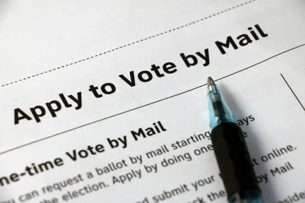 Closeup on heading, 'Apply to Vote by Mail' with text below, black print on white paper, and pen laying on top.