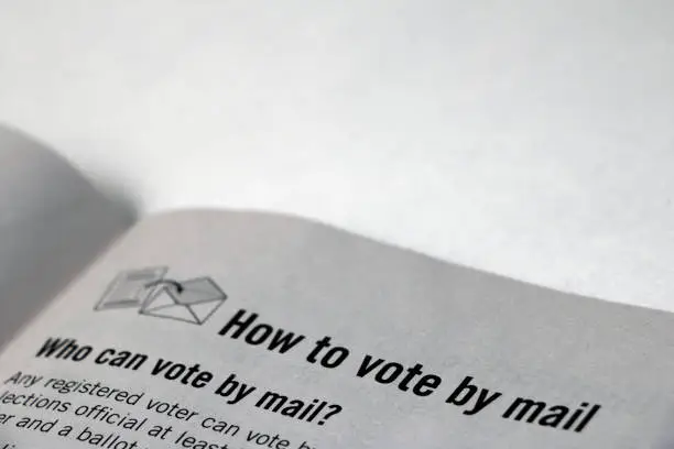 Closeup of top of a booklet page, focused on heading 'How to vote by mail' with 'Who can vote by mail?' text below, black print on off-white paper.