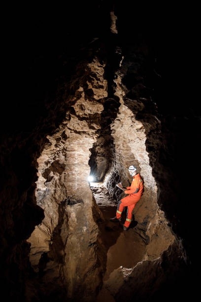 istock Man walking and exploring dark cave with light headlamp and map in his hand underground. Mysterious deep dark, explorer discovering mystery moody tunnel looking on rock wall inside. 1250126736