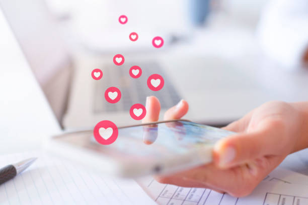 Woman using mobile phone and getting lots of likes. Woman using mobile phone and getting lots of likes. Social media influencer concept. There is also a laptop in the background and some paperwork on the table. She is at work in the office persuasive stock pictures, royalty-free photos & images