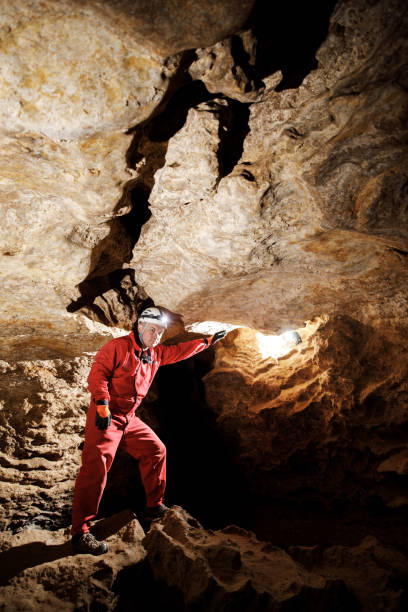 istock Man walking and exploring dark cave with light headlamp underground. Mysterious deep dark, explorer discovering mystery moody tunnel looking on rock wall inside. 1250127919