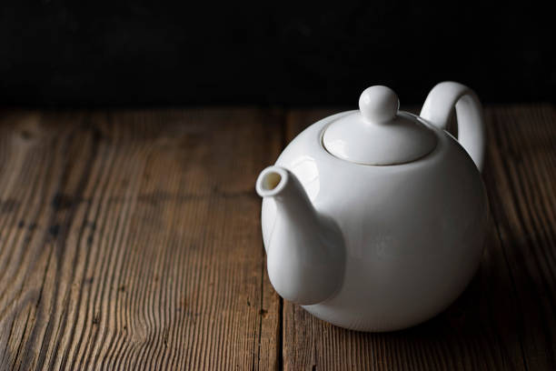 istock White ceramic mockup teapot for hot drinks on empty old wooden table near black wall in evening light with shadows. Horizontal with copy space for text and design. Rustic style. 1250128508