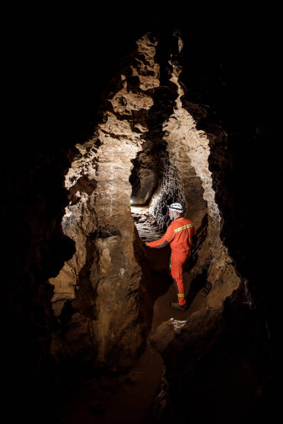 istock Man walking and exploring dark cave with light headlamp underground. Mysterious deep dark, explorer discovering mystery moody tunnel looking on rock wall inside. 1250129386