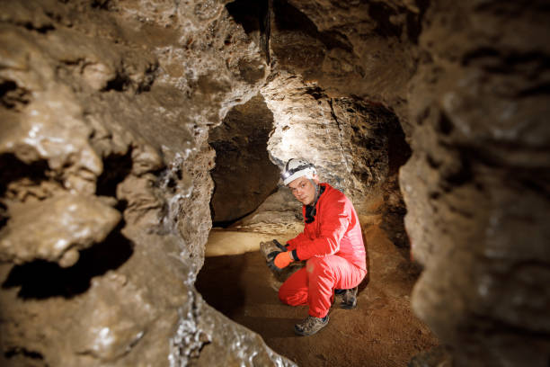 istock Man walking and exploring dark cave with light headlamp underground. Mysterious deep dark, explorer discovering mystery moody tunnel looking on rock wall inside. 1250130242