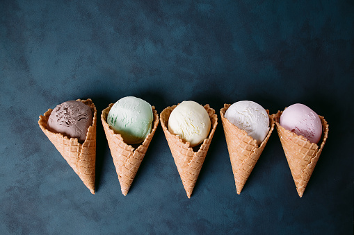 Set of ice cream cones of different colors and flavors on dark table, copy space. Food background, summer refreshing concept, traditional seasonal cold sweets