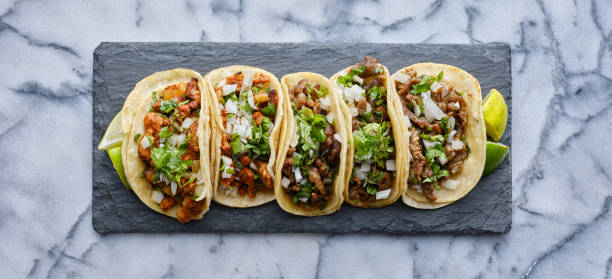 row of mexican street tacos on slate with carne asada and al pastor in corn tortilla row of mexican street tacos on slate with carne asada and al pastor top down taco photos stock pictures, royalty-free photos & images