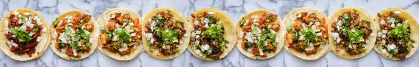 row of mexican street tacos with carne asada and al pastor in corn tortilla wide banner composition