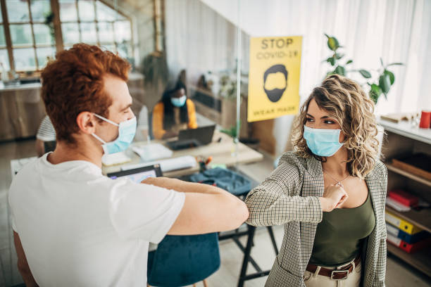 istock Man and woman with protective masks greeting with elbows in office 1250137948