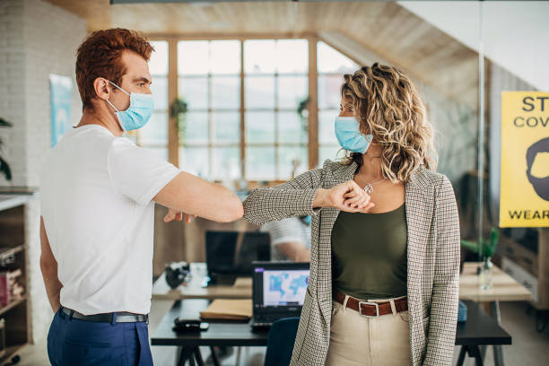 istock Man and woman with protective masks greeting with elbows in office 1250138112