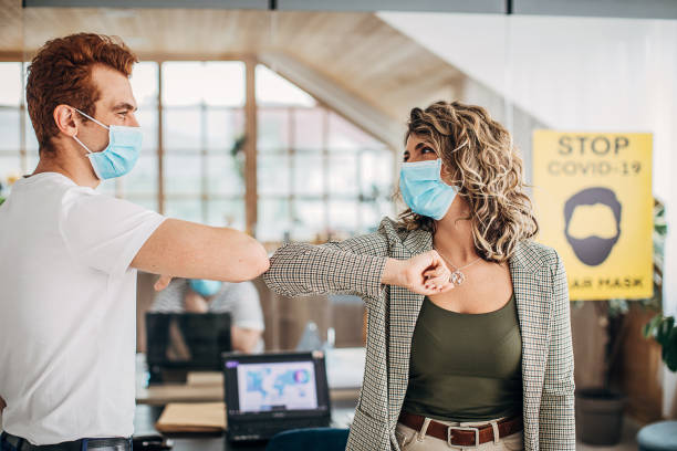 istock Man and woman with protective masks greeting with elbows in office 1250138121