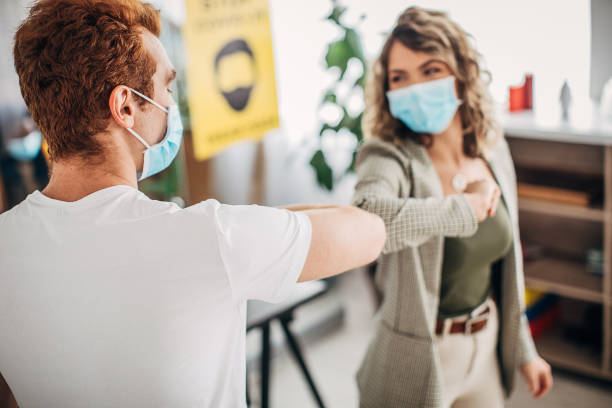 istock Man and woman with protective masks greeting with elbows in office 1250138132