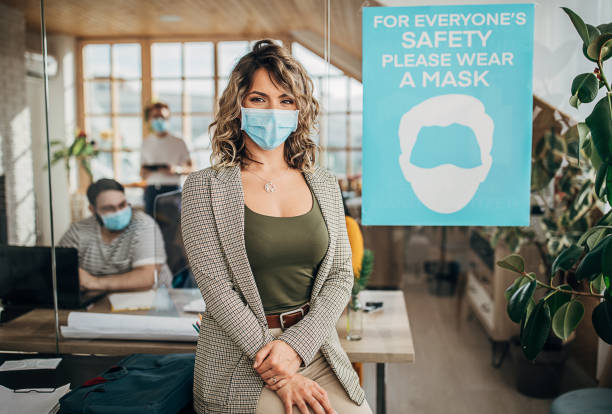 istock Beautiful woman with protective mask standing in office 1250138166