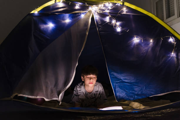istock Boy inside the tent reading a book at night 1250139148