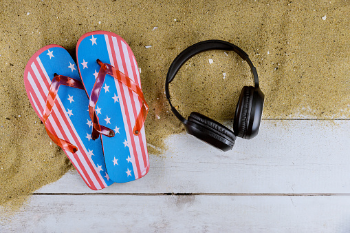 American flag new flip flops beach slippers sand beach headphones on old wooden background