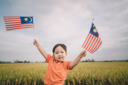 malaysia independence day an asian chinese young boy waving with malaysia flag at padi field enjoying morning sunlight and feel proud and happy