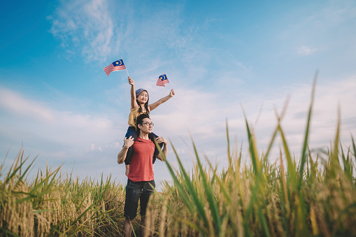malaysia independence day an asian chinese young girl holding malaysia flag at padi field carried by her father on her father shoulder enjoying morning sunlight and feel proud and happy
