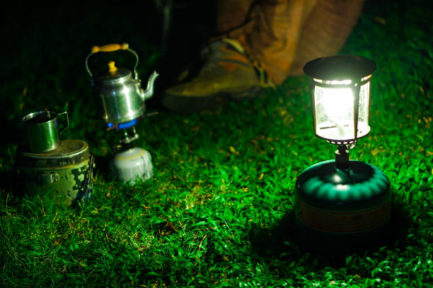 gaslampe und wanderschuhe auf grünem rasen. blurred aluminum kettle auf dem gas-camping-herd auf der rückseite. camping in nature.shallow fokuseffekt. - hand tool glass metal condition stock-fotos und bilder