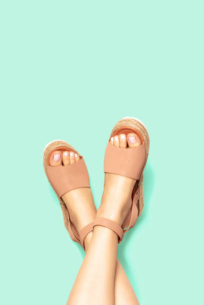 patas femeninas con pedicura blanca en sandalias marrones de verano sobre fondo, espacio de copia - sandalia fotografías e imágenes de stock
