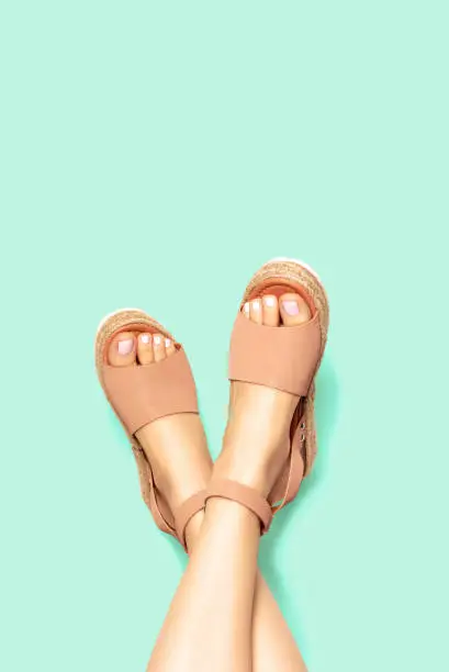 Female legs with a white pedicure in summer brown sandals on background, copy space