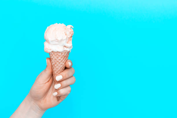 istock A woman's holds an ice cream cone on blue background, view from the front, 19th World Ice Cream Day 1250160189
