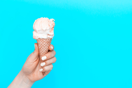A woman's holds an ice cream cone on a blue background, view from the front, 19th World Ice Cream Day