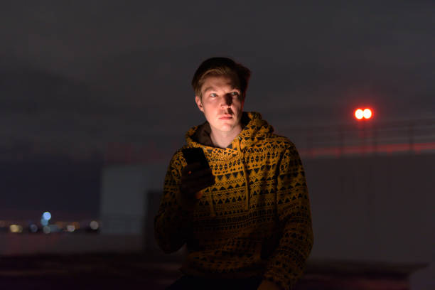 istock Young handsome man thinking while using phone at rooftop of the building during stormy weather at night 1250164191