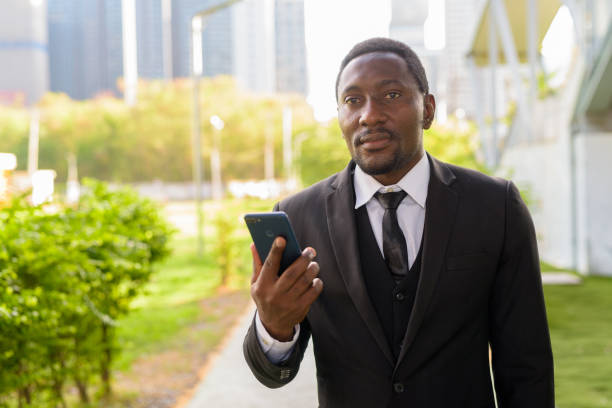 istock Handsome bearded African businessman thinking while using phone at the park 1250165114
