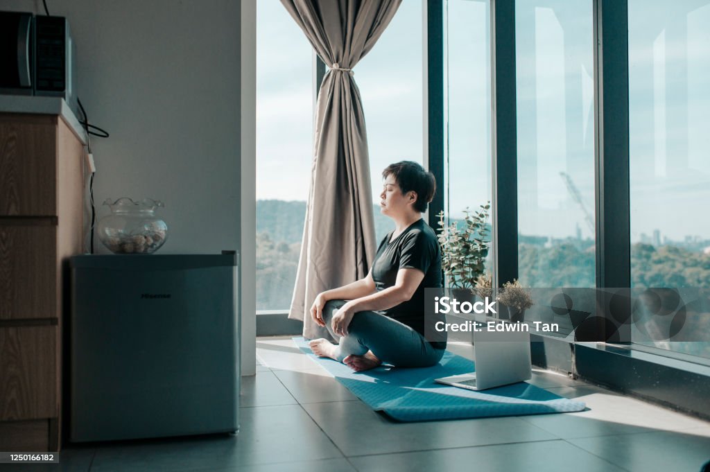 an asian chinese beautiful woman workout at home mediating on yoga mat at kitchen corner near the window on weekend morning an asian chinese beautiful woman workout at home mediating on yoga mat at kitchen corner near the window on weekend Zen-like Stock Photo