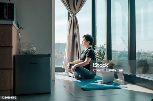 An Asian Chinese Beautiful Woman Workout At Home Mediating On Yoga Mat At Kitchen Corner Near The Window On Weekend Morning Stock Photo - Download Image Now