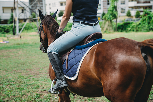 Young adult woman riding a horse at the riding school. She's training and learning how to ride a horse.