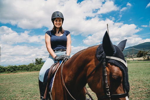 Young adult woman riding a horse at the riding school. She's training and learning how to ride a horse.