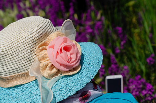 Back view of woman in a straw hat with a flower pattern is looking at the mobile phone in flowers