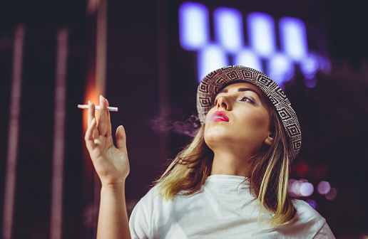 Young pretty Caucasian hipster woman with cigarette downtown at night.