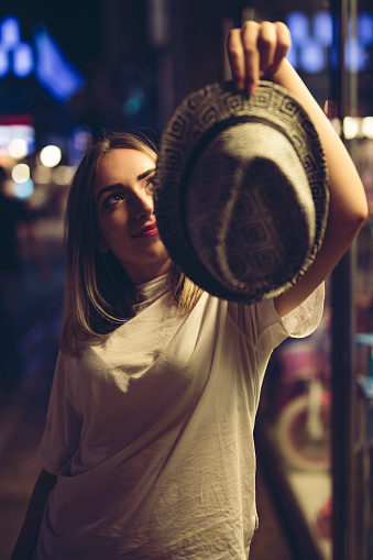 Young beautiful Caucasian woman with hat on a city street at night.
