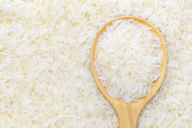 Thai jasmine rice Thai jasmine rice in wooden spoon over rice background. jasmine rice stock pictures, royalty-free photos & images