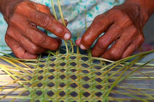 close detail of a pair of hands weaving a traditional basket