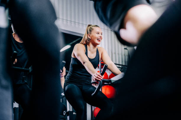 Smiling sporty woman cycling at health club Confident female cycling at health club. Sporty woman is in stationary cycling class. She is in sportswear. spin bike stock pictures, royalty-free photos & images
