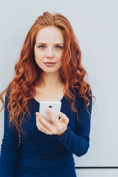 istock Young red-haired woman holding mobile phone 1250191302