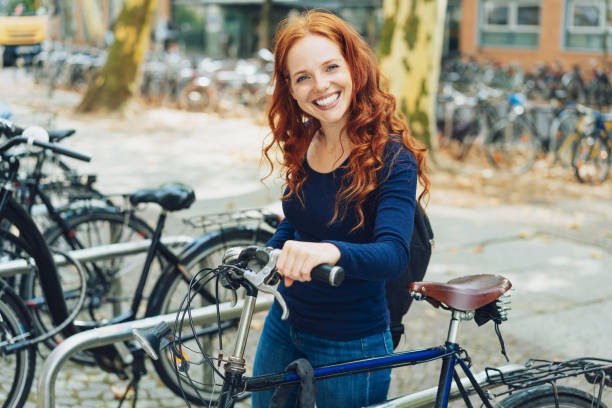 pretty young redhead student parking her bike - cycling bicycle women city life imagens e fotografias de stock