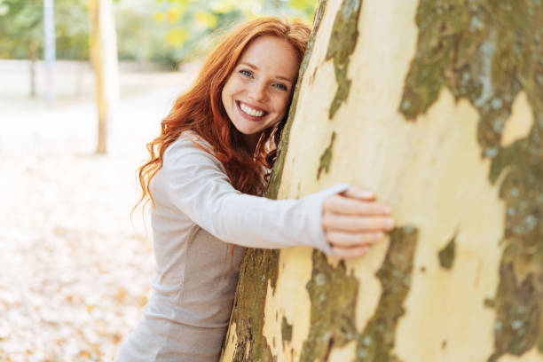 pretty redhead woman hugging a large tree