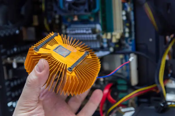 Photo of caucasian hand holding orange plated computer heatsink and pc internals in blurry background