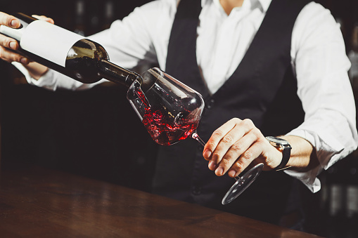 Close-up photo, sommelier pours red wine to glass on bar counter background. Bartender, degustation of alcoholic beverage.
